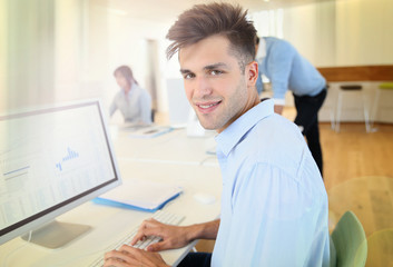 Naklejka na ściany i meble Office worker sitting in front of desktop, colleagues in background