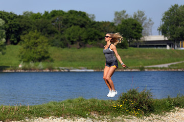 Blonde fitness girl jump roping at a river bank