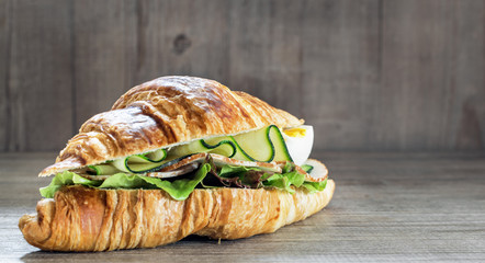 Chicken ham and  egg breakfast sandwich on a croissant on a rustic wooden board. Selective focus.