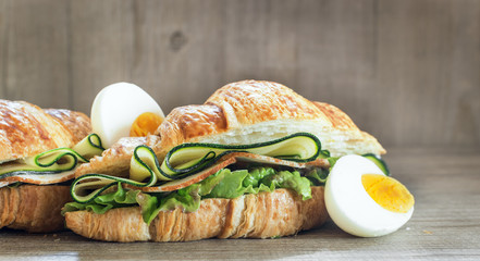 Chicken ham and  egg breakfast sandwich on a croissant on a rustic wooden board. Selective focus.