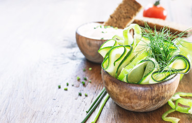 Tzatziki sauce in wooden bowl, with ingredients - cut cucumber, mint, dill on a dark wooden background with free text space. selective focus.