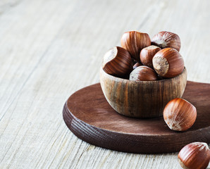 Hazelnuts in wooden bowl on dark brown board. Selective focus.