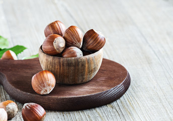 Hazelnuts in wooden bowl on dark brown board. Selective focus.