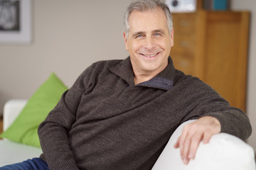 sympathischer best-ager sitzt zuhause auf dem sofa