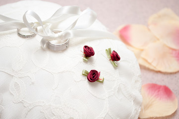 Two wedding rings sit on top of a delightful ring cushion with flower petals in the background.