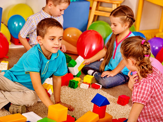 Group children game blocks on floor in kindergarten . Children play together.