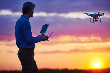 man operating of flying drone at sunset - obrazy, fototapety, plakaty