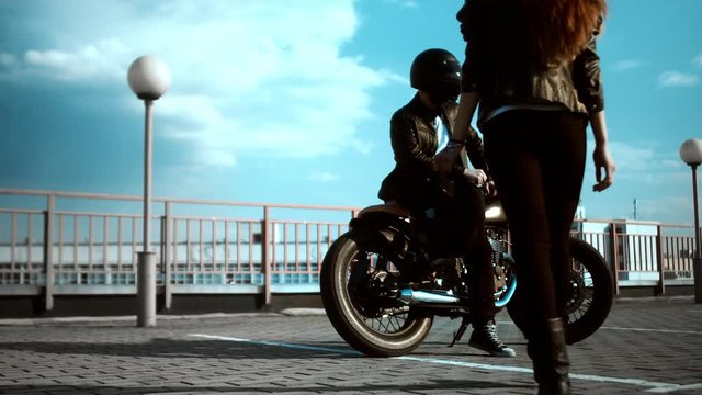 Young woman walking towards man on motorcycle