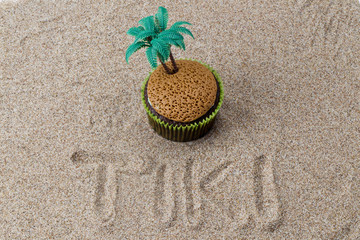 image of cupcake with plastic coconut tree with tiki inscribed in the sand.