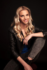  smiling blonde woman in leather jacket resting on a chair
