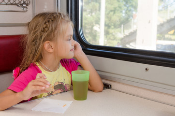 Six-year girl sitting on the train at the table on outboard second-class carriage and...