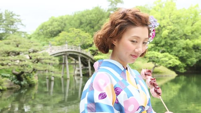 日本庭園で団子を食べる着物女性