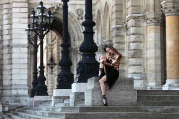 Fototapeta na wymiar Sad ballerina in black skirt, haze and golden top sitting in front of a palace