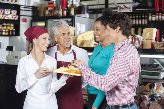 Salespeople Offering Cheese Samples To Customers In Shop