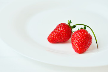 Two red strawberries on a white plate. Strawberries on white background 
