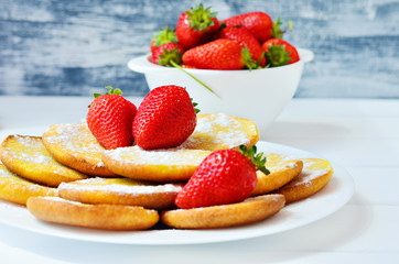 Pancakes with powdered sugar and a strawberry on a wooden background 