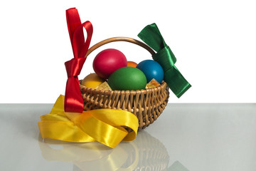 Easter Wicker basket with pink vines painted chicken eggs on a white background and on the basis of reflective matte decorated with colorful ribbons.