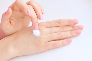 Young woman with pink manicure applies cream on her hands