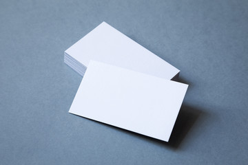 Stack of thick blank business cards on a grey background, top view. The top card is shifted to...