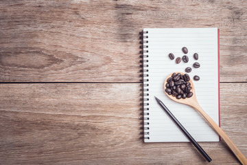 Coffee beans and and lined paper on wooden table top view