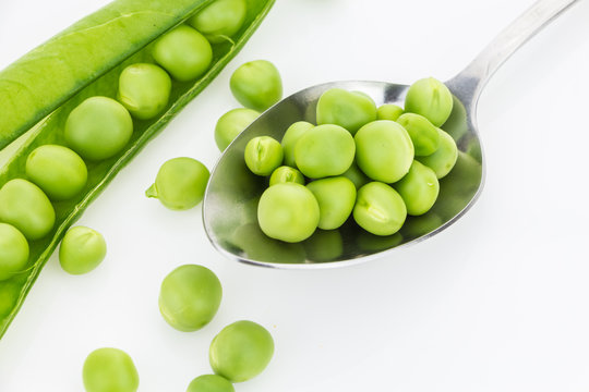 Fresh green peas in spoon closeup and a pea pod, on white background