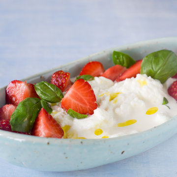 Creamy stracciatella with strawberries, basil and olive oil. Selective focus.