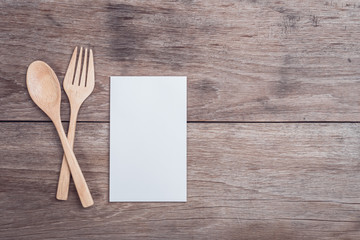 Wooden spoon, fork and blank paper on wooden table top view