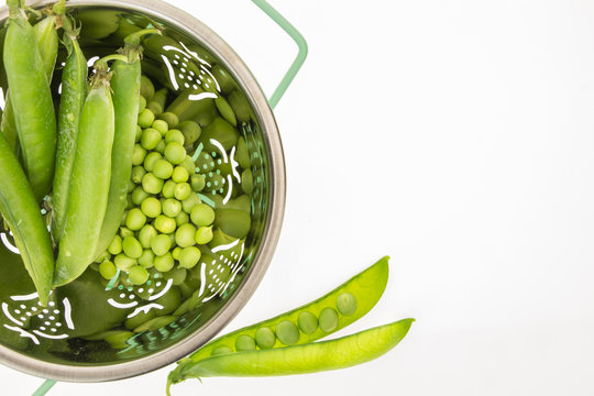 Fresh green peas in colander, on white background with copy-space