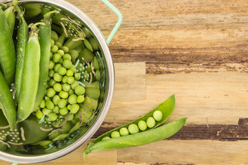 Fresh green peas in colander, on wooden surface