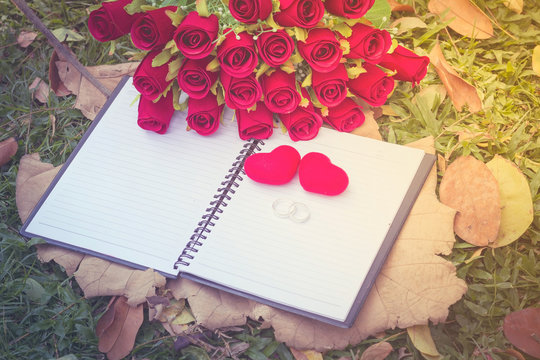 wedding rings , wedding bouquet of red roses and heart shape on white notebook space for your text. decoration idea love concept for valentines day