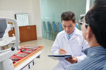 Vietnamese optometrist reading medical card of male patient