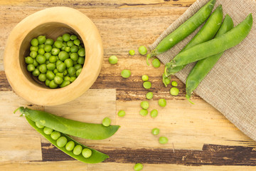 Fresh green peas in wooden bowl, on wooden surface and cloth