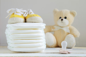 Some nappies on a white wooden table. Sneakers, a pacifier and a teddy bear. Empty copy space for...