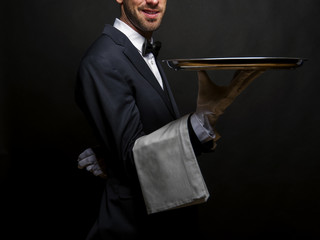 Waiter in black suit holding tray over black background. - Powered by Adobe