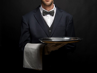 Waiter in black suit holding tray over black background. - obrazy, fototapety, plakaty