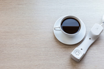 White coffee cup and office phone on wooden table