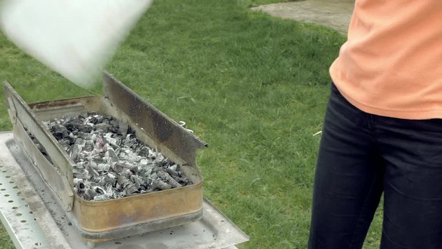 Girl blows coals and fans embers in the barbecue bbq brazier. Outdoors picnic concept. 4K UHD video footage.