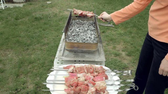 Girl puts barbecue bbq skewers with red meat on brazier with hot coals embers. Outdoors picnic concept. 4K UHD video footage.