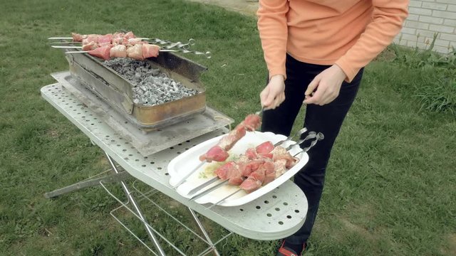 Girl puts barbecue bbq skewers with red meat on brazier with hot coals embers. Outdoors picnic concept. 4K UHD video footage.