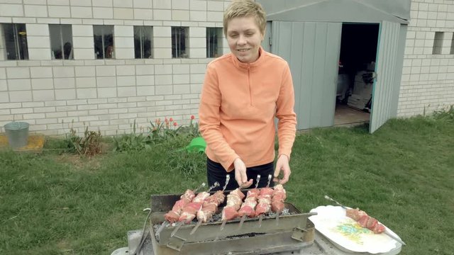 Girl puts barbecue bbq skewers with red meat on brazier with hot coals embers. Outdoors picnic concept. 4K UHD video footage.