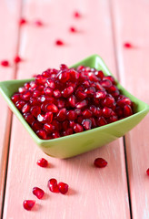 pomegranate seeds in a bowl on wooden surface