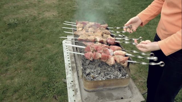 Girl cooks barbeque skewers with meat on hot coal ember brazier Outdoors picnic concept. 4K UHD video footage.
