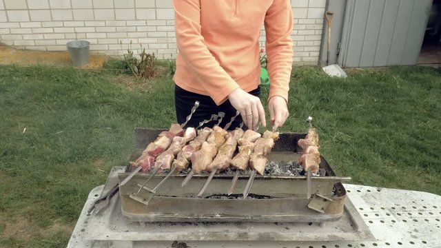 Girl cooks barbeque skewers with meat on hot coal ember brazier Outdoors picnic concept. 4K UHD video footage.
