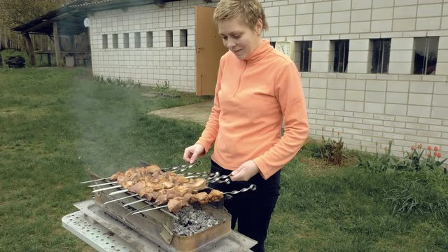 Girl cooks barbeque skewers with meat on hot coal ember brazier Outdoors picnic concept. 4K UHD video footage.