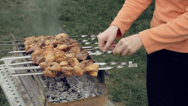 Girl cooks barbeque skewers with meat on hot coal ember brazier Outdoors picnic concept. 4K UHD video footage.