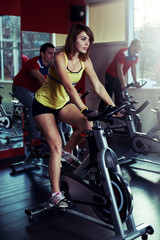 Cycling girl in sportswear training in the gym. Sporty people working out on spinning machines in fitness club.