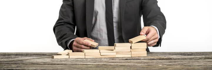 Businessman arranging wooden pegs into a staircase like structur