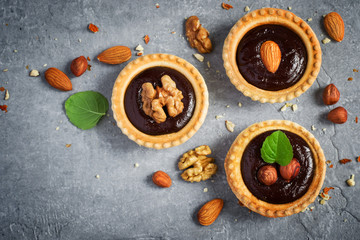 Small Chocolate Tarts decorated with different nuts on a gray st
