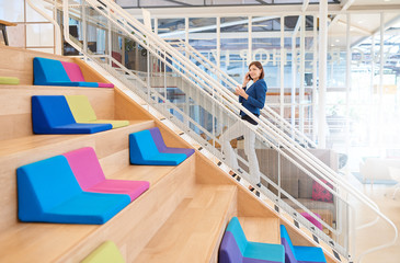 Businesswoman on phone walking up stairs with takeaway coffee