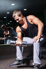 Fototapeta na wymiar Smiling bodybuilder doing exercise on biceps with dumbbell
